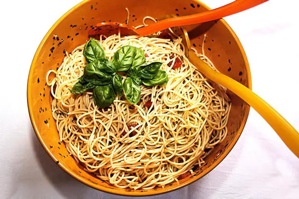 A bowl of instant Chinese noodles with green onions, red hot chilli peppers, and carrots, shot from above on a dark texture with chopsticks and a place for text